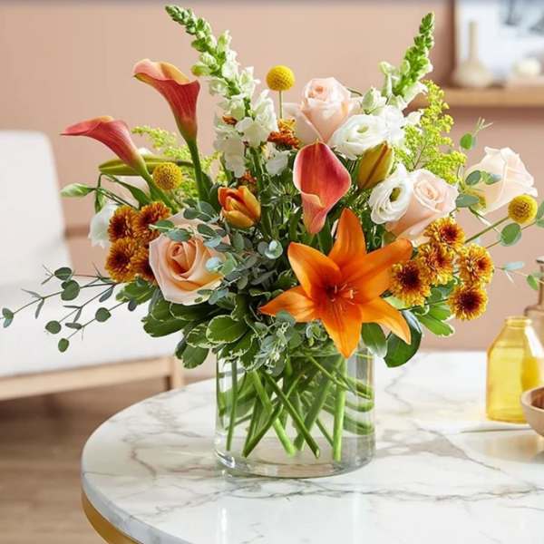 Mixed bouquet of orange lilies, roses, and white blooms in a glass vase