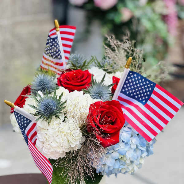 Red roses and hydrangeas in a white vase with small American flags