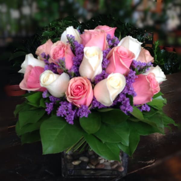 Pink and white roses arranged in a square glass vase with purple filler