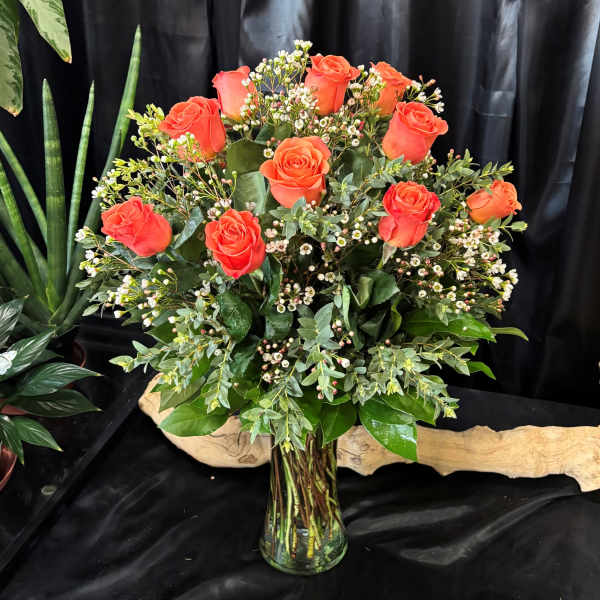 Orange roses arranged in a clear glass vase with small white filler flowers