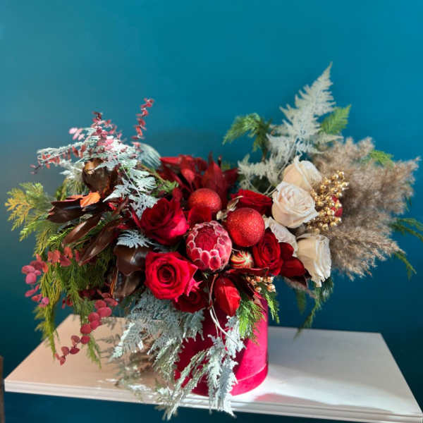 Red and white rose arrangement in a pink hat box with decorative accents