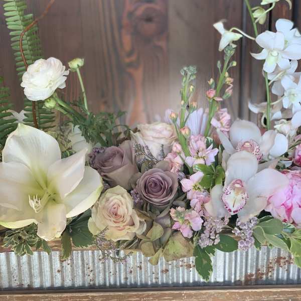 Pastel floral arrangement with white lilies, roses, and orchids in a rustic container