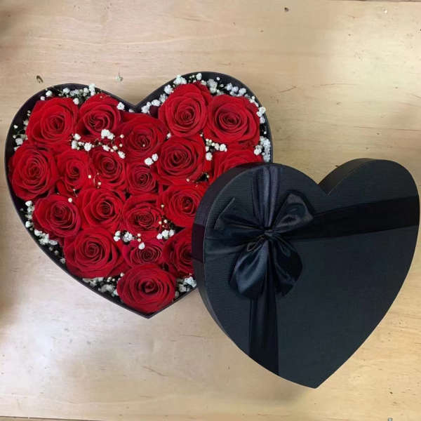 Heart-shaped box of red roses with white filler flowers and a black ribbon bow