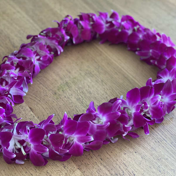 A purple orchid lei laid in a loop on a wooden surface.