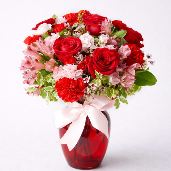 Red roses and pink carnations in a red glass vase with a pink ribbon