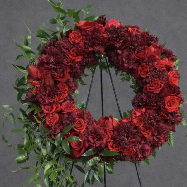 Red floral wreath on a black stand with trailing greenery