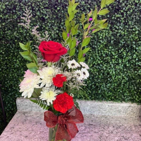 Red roses and white daisies in a glass vase with a red bow