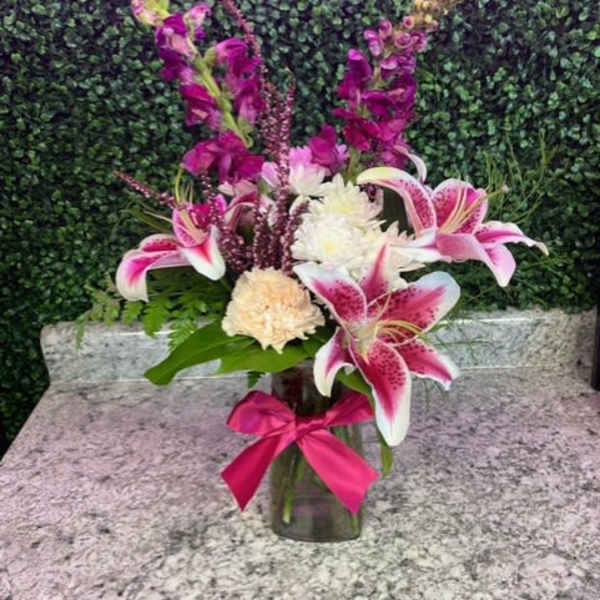 Pink lilies and purple flowers arranged in a glass vase with a ribbon