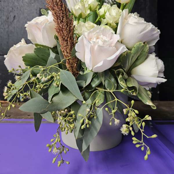 White tulips and pale roses in a round vase with trailing greenery