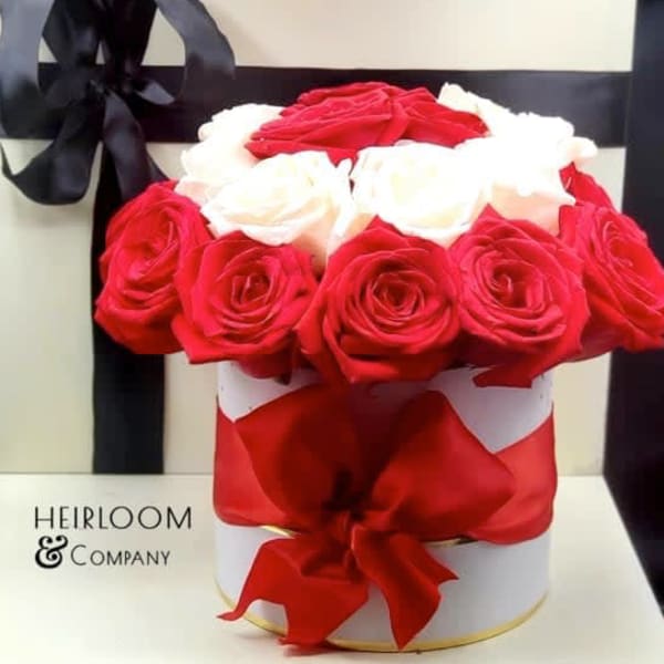 Red and white roses arranged in a round gift box with a black ribbon