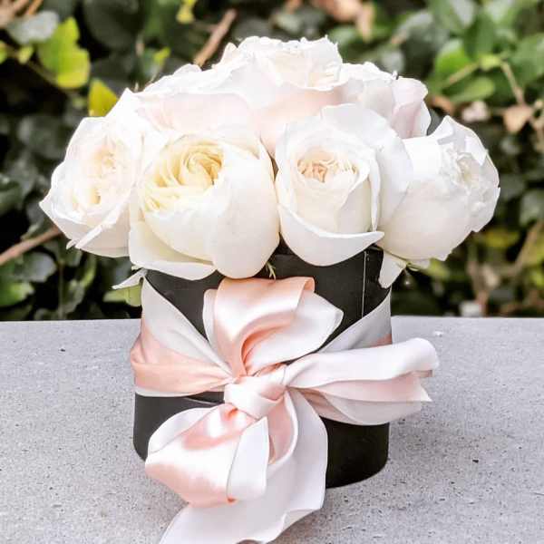 White roses in a black box tied with a pink satin ribbon
