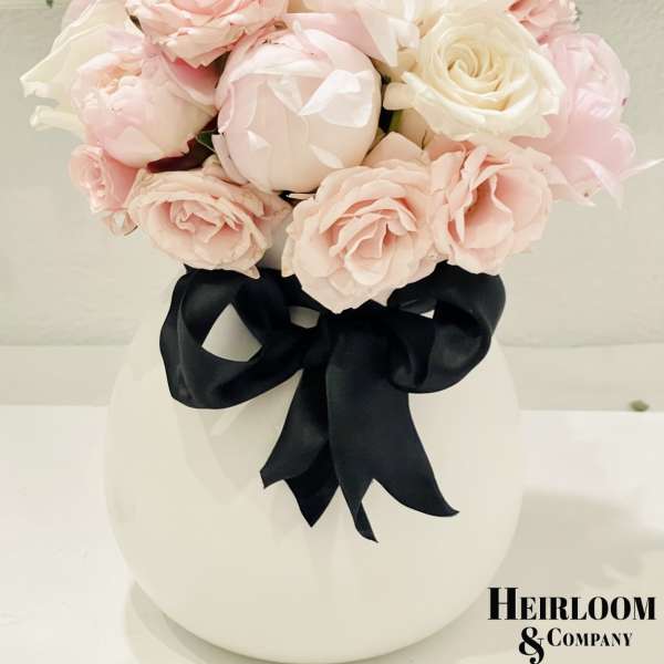 Blush pink and white roses in a white vase with a black ribbon