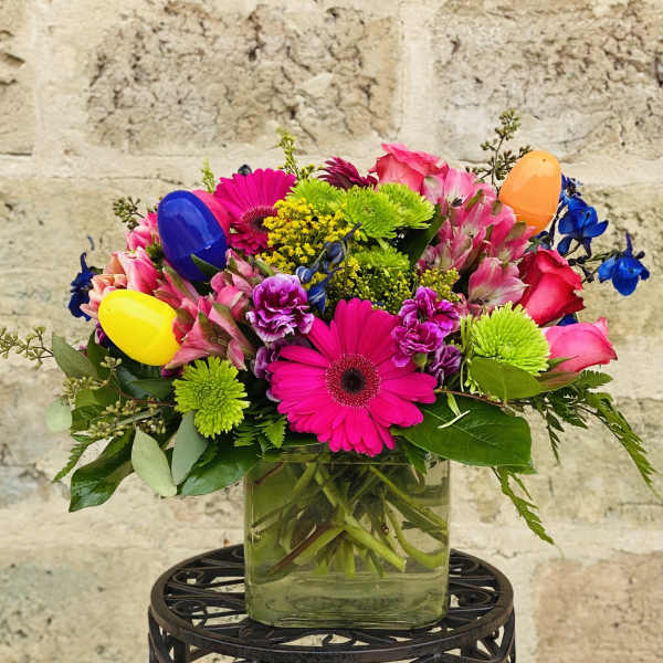 Bright mixed bouquet in a glass vase with colorful plastic eggs
