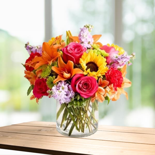 Mixed bouquet of roses, lilies, and sunflowers in a glass vase