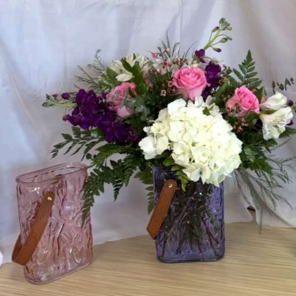 Pink and white flower arrangement in a purple glass vase with two matching gift bags