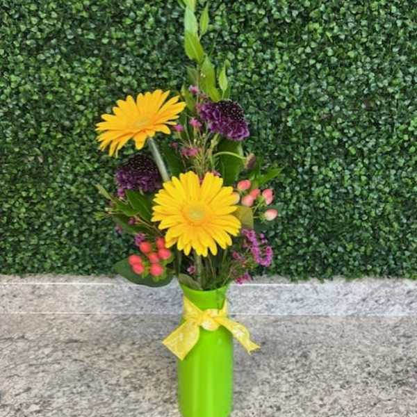 Yellow gerbera daisies in a green vase with purple accents