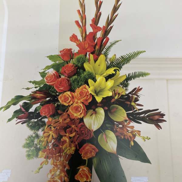 Tall tropical floral arrangement with red roses, yellow lilies, and orange orchids
