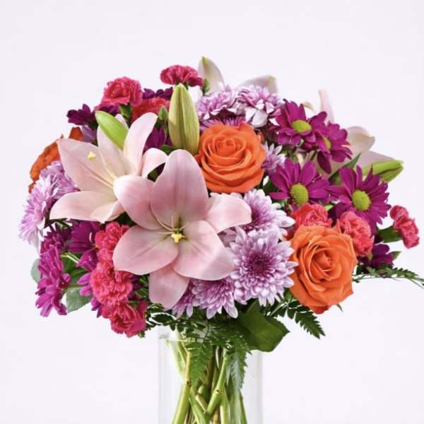 Mixed pink, purple, and orange flowers in a clear glass vase
