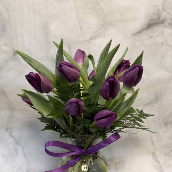 Purple tulips arranged in a clear glass vase with a purple ribbon.