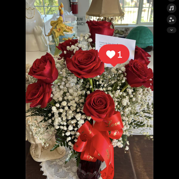 Arrangement of red roses and white filler flowers in a red glass vase with a red love ribbon