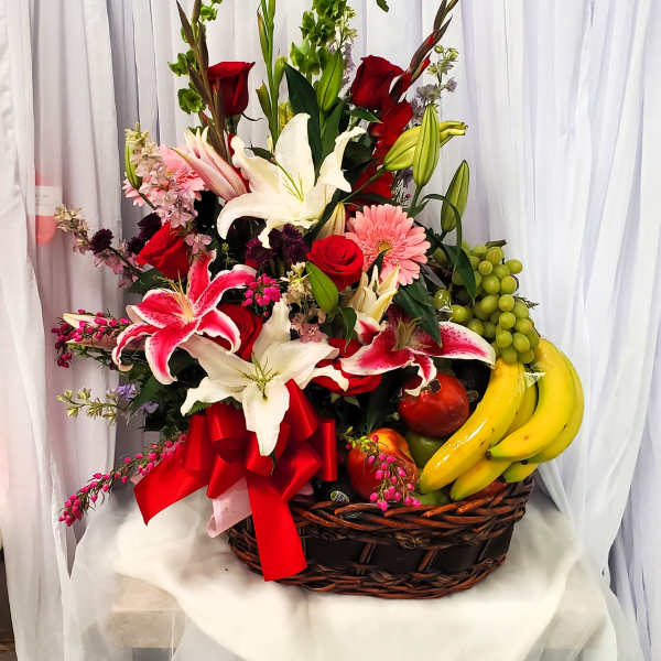 Basket arrangement of lilies, roses, and fruit with a red ribbon