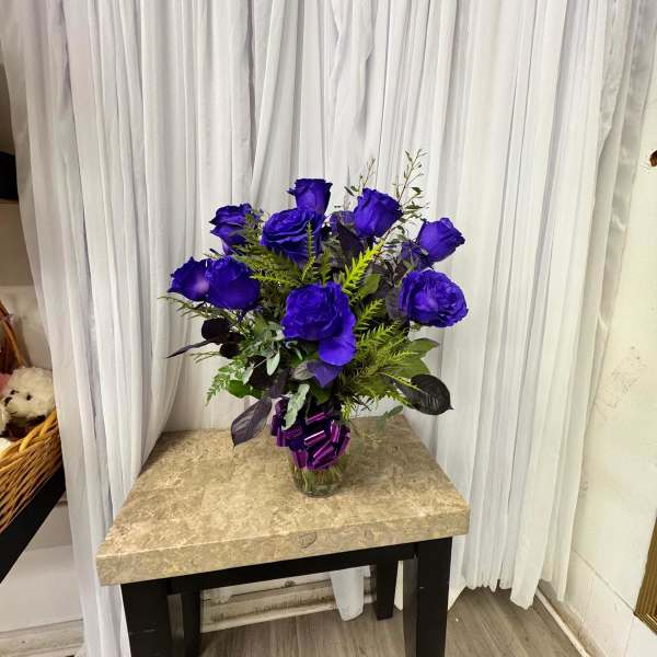 Blue rose bouquet in a glass vase with a purple ribbon