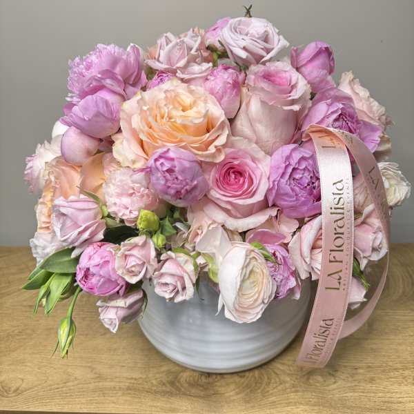 Pink and peach roses arranged in a white vase with a ribbon