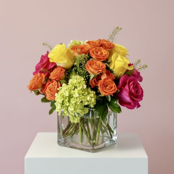Bouquet of orange, yellow, and pink roses in a clear square vase