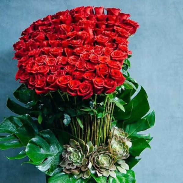 Large red rose arrangement in a tall green vase with succulents