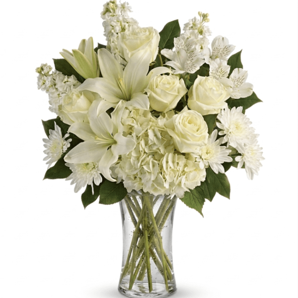 All-white bouquet of lilies, roses, hydrangeas, and other blooms arranged in a clear glass vase