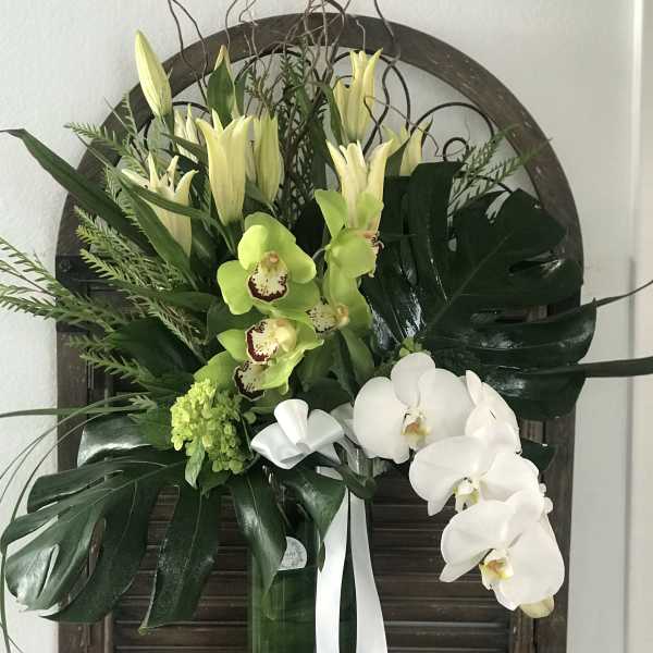 Tall floral arrangement with white orchids and green lilies in a vase