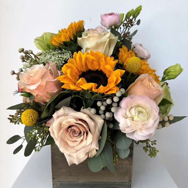 Mixed bouquet with sunflowers, roses, and pale pink blooms in a wooden box