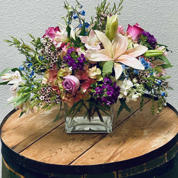 Mixed bouquet in a square glass vase with pink, white, and purple flowers