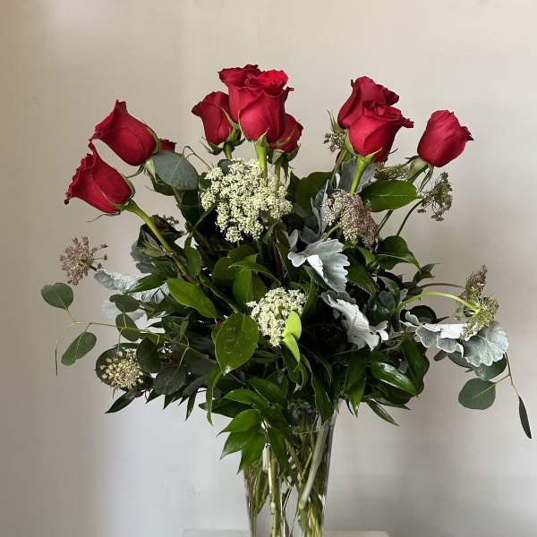 Red roses arranged in a clear glass vase with mixed greenery