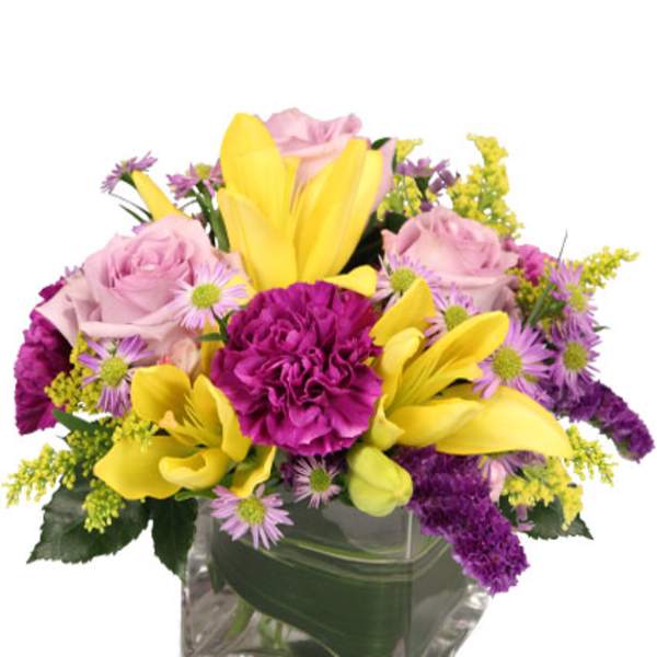 Mixed bouquet of yellow lilies, pink roses, and purple flowers in a glass vase