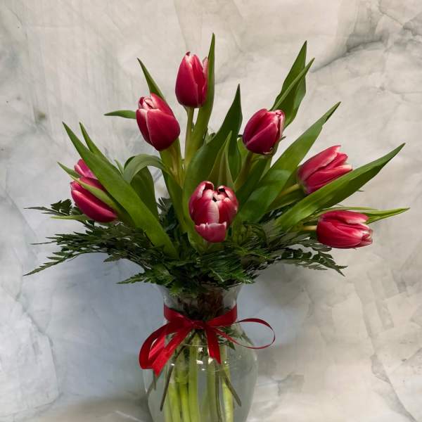 Pink tulips arranged in a clear glass vase with a red ribbon