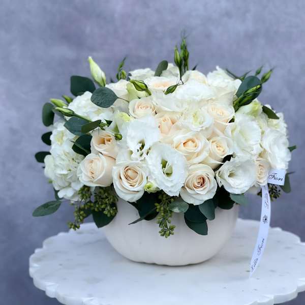 White roses and lisianthus arranged in a white bowl vase