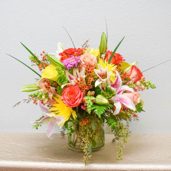 Mixed bouquet of roses, lilies, and yellow blooms in a glass vase
