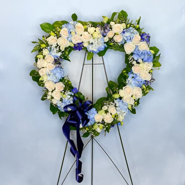 Heart-shaped floral wreath with white and blue flowers on a stand