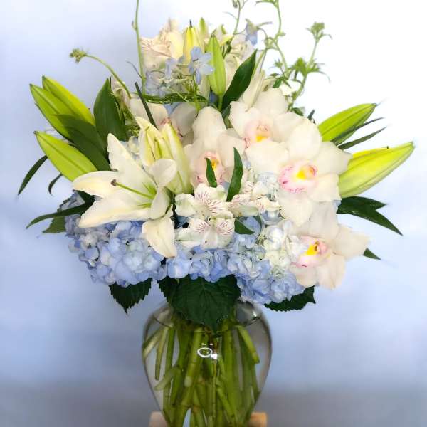 White lilies and orchids in a glass vase with blue hydrangeas