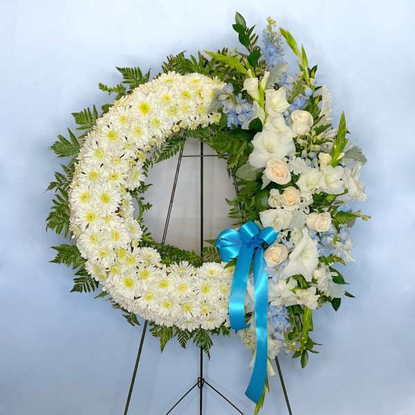 White floral wreath on a stand with a blue ribbon