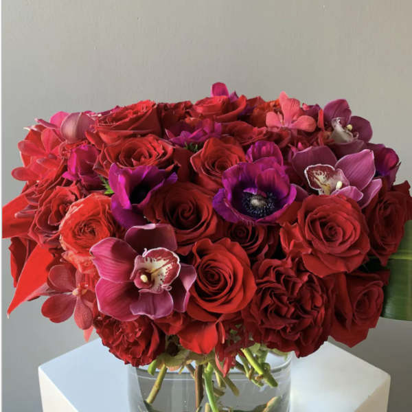 Red and pink bouquet of roses and orchids in a clear glass vase