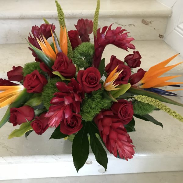 Tropical arrangement of red roses and orange bird-of-paradise blooms in a low container