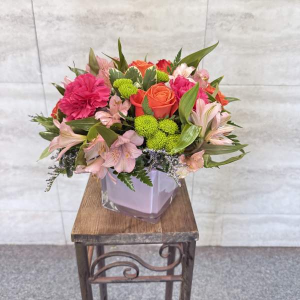 Mixed pink and orange flowers arranged in a square glass vase