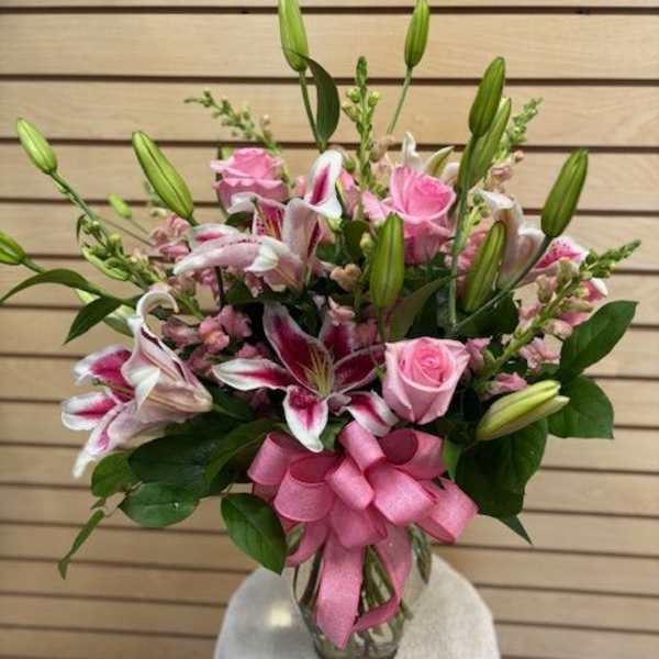 Pink roses and lilies arranged in a glass vase with a ribbon