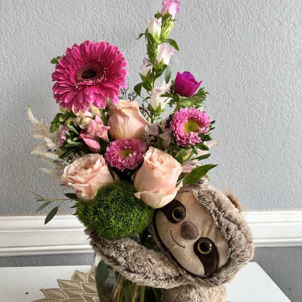 Pink flower arrangement with a plush sloth in a glass vase
