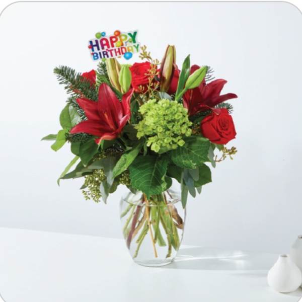 Red lilies and roses in a glass vase with a Happy Birthday pick