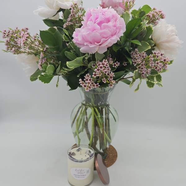 Pink and white flowers in a glass vase with a candle in front