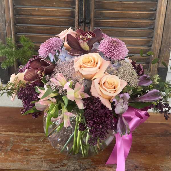 Mixed bouquet of peach roses, orchids, and purple blooms in a glass vase