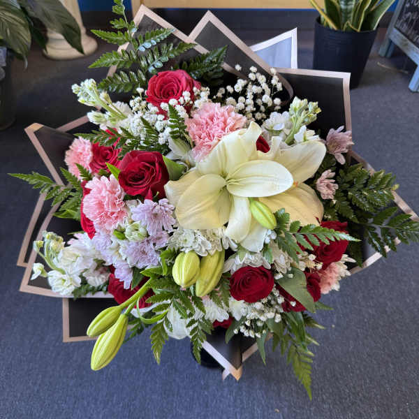 Bouquet of red roses, white lilies, and pink carnations wrapped in black paper